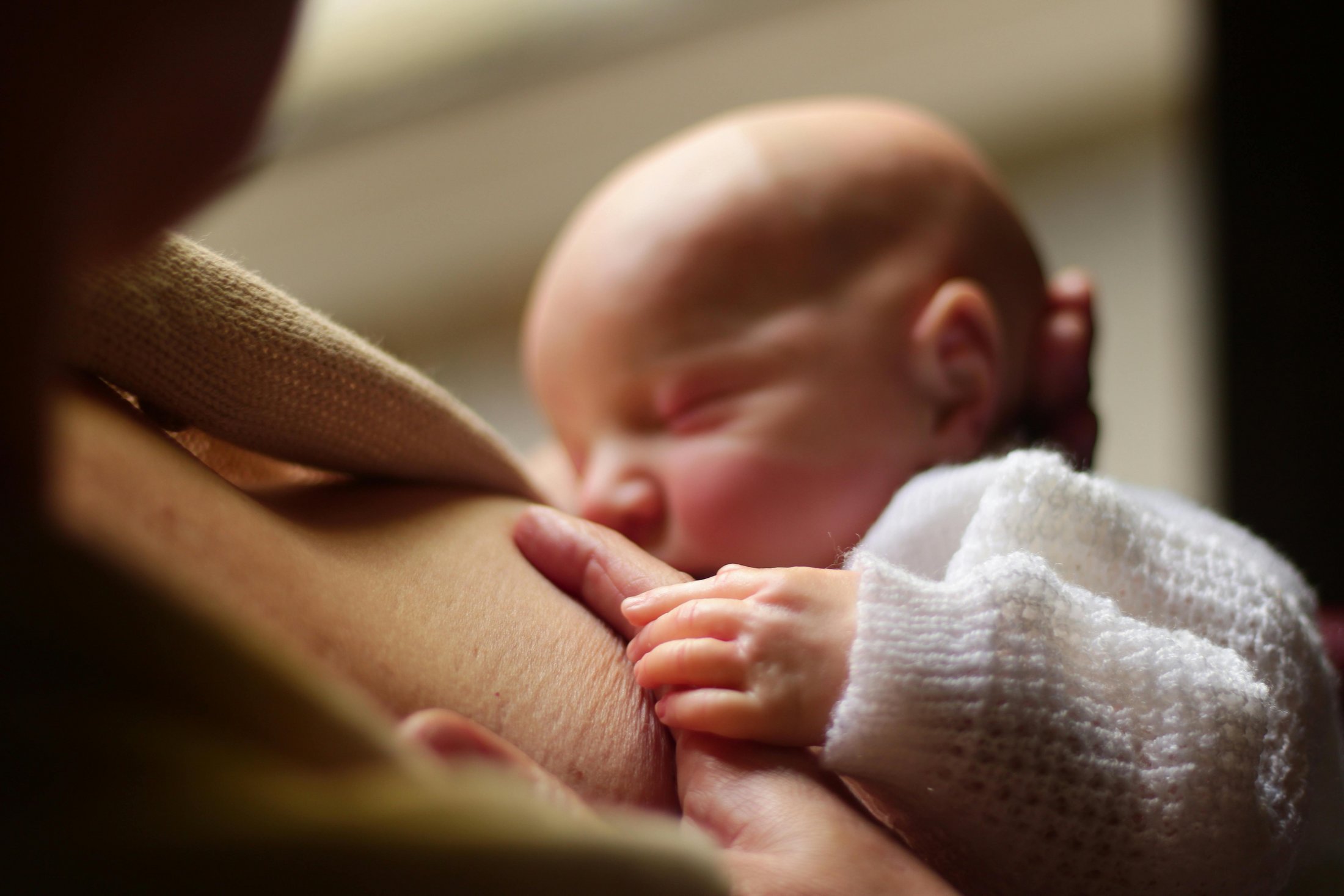 A close-up of a newborn breastfeeding, gently holding the parent’s skin while feeding.