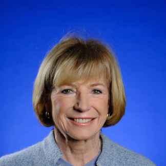 Portrait of Dr. Dominique Haumont smiling in front a blue background.