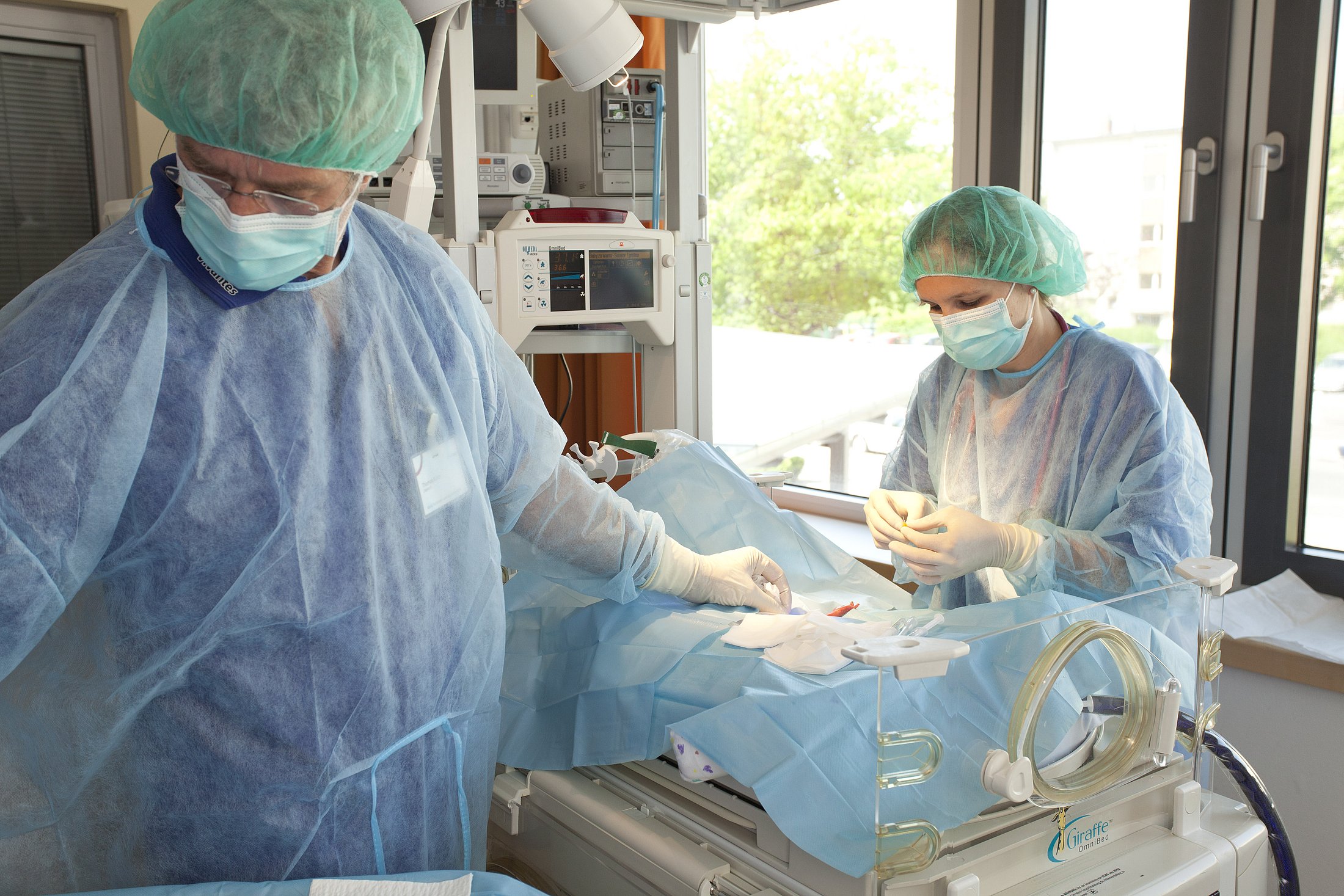 Specialized Care for a Preterm Infant Two healthcare professionals wearing protective clothing care for a preterm infant in a neonatal unit.
