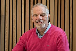 Portrait of Professor Dieter Wolke smiling in a red sweater in front of a striped wall.