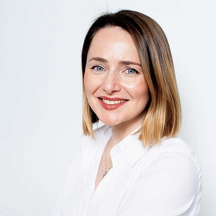 Portrait of Oleksandra Balyasna smiling in a white blouse in front of a neutral background.