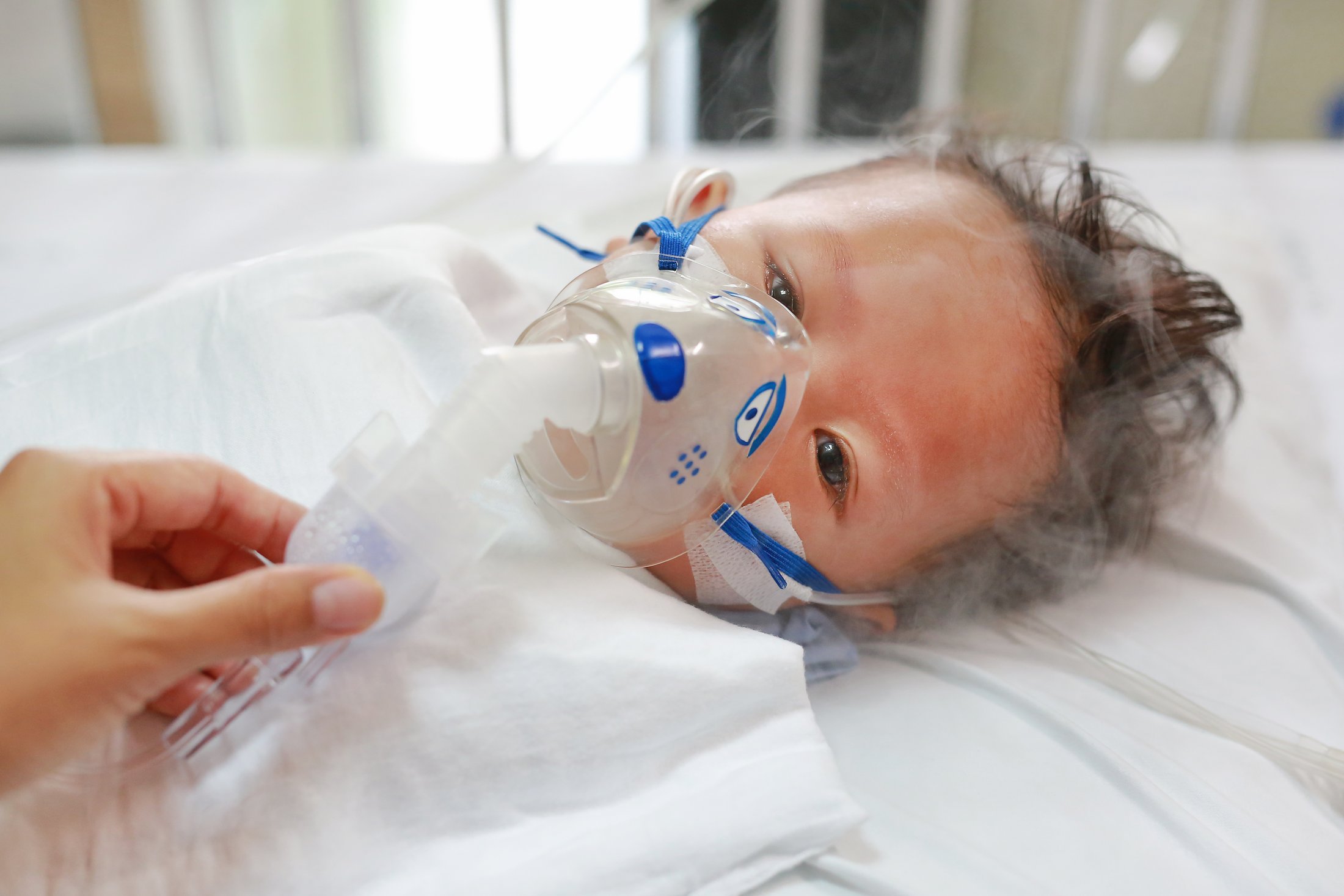 RSV Prevention and Treatment in Newborn Infants A young child lies in a hospital bed receiving oxygen therapy through a nebulizer mask, illustrating the importance of RSV prevention and respiratory care.