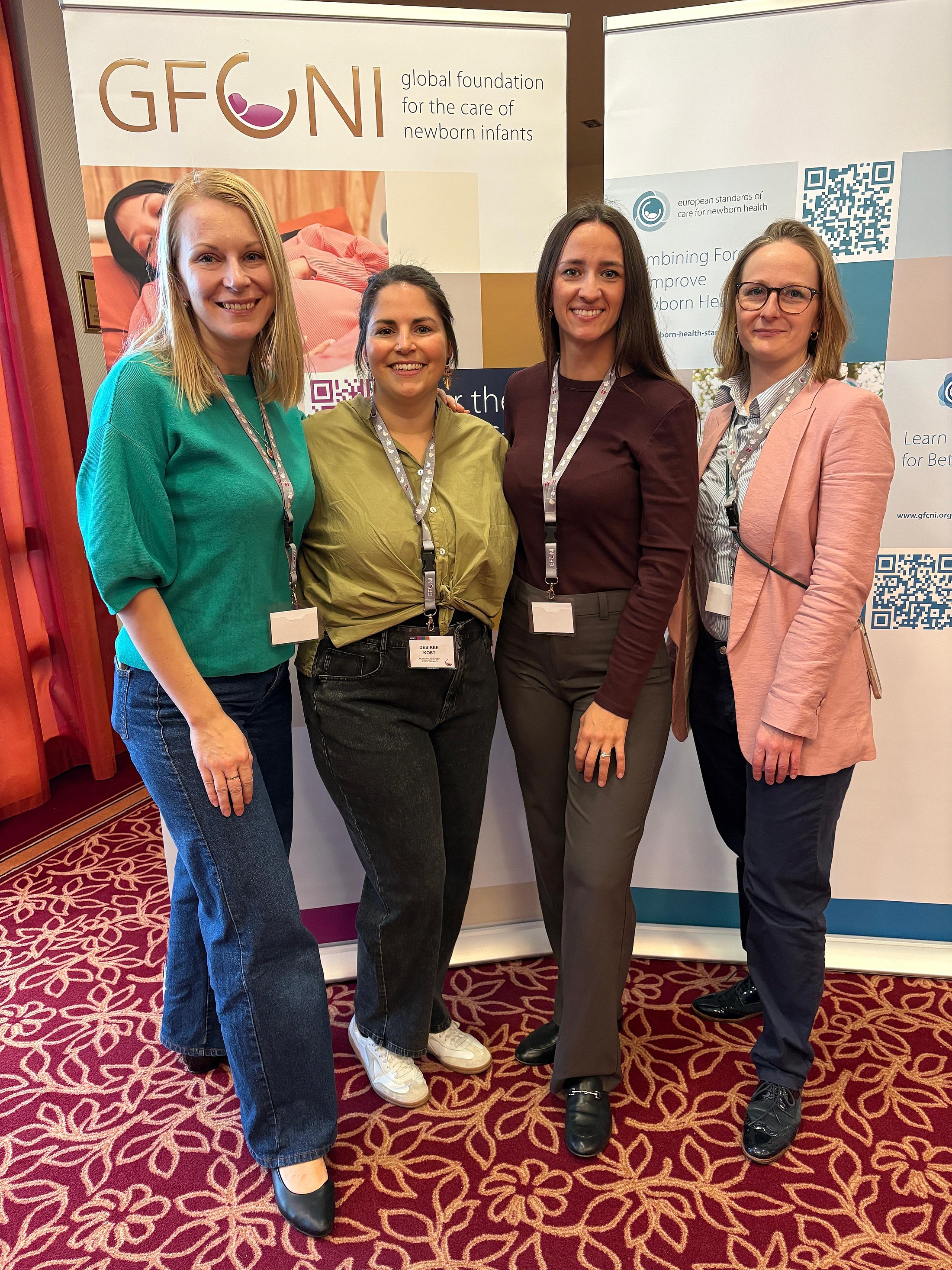 Four participants posing together in front of GFCNI and European Standards of Care for Newborn Health banners at an international event.