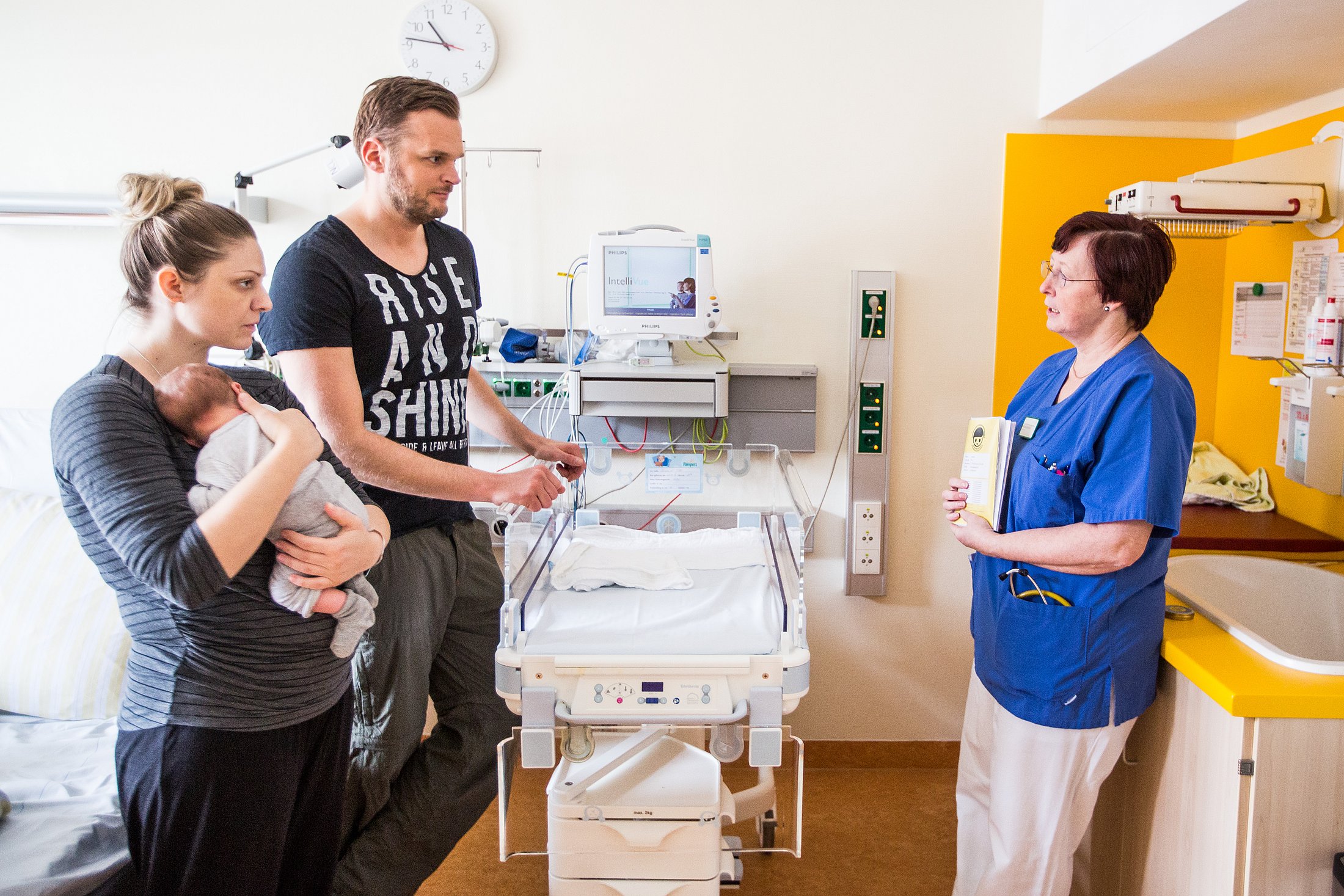 Parents Receiving Guidance in the Neonatal Unit Neonatal nurse speaks with a mother holding her infant and the baby’s father beside a neonatal care cot.