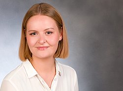 A professional headshot of Ruth Kemper, wearing a white blouse against a grey background.