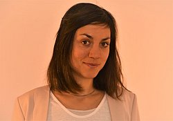 A professional headshot of Dr. Julia Hoffmann in a light peach blazer against a warm-toned background.