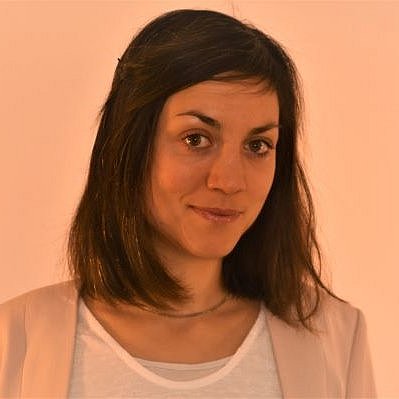 A professional headshot of Dr. Julia Hoffmann in a light peach blazer against a warm-toned background.