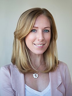 A professional portrait headshot of Laura Staudt wearing a rosa blazer and necklace.