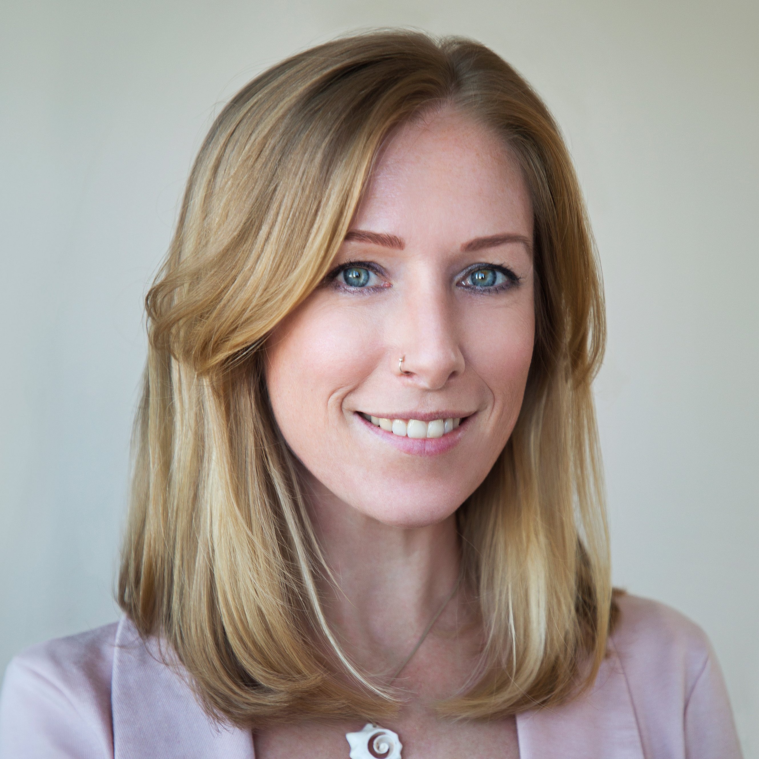 A professional portrait headshot of Laura Staudt wearing a rosa blazer and necklace.