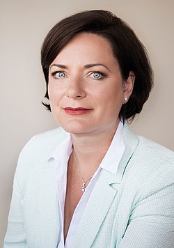 A professional headshot of Nicole Thiele, smiling in a soft green blazer and white blouse.