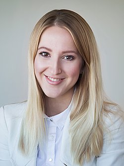 A professional headshot of Diana Hofmann-Larina, smiling in a white blazer.