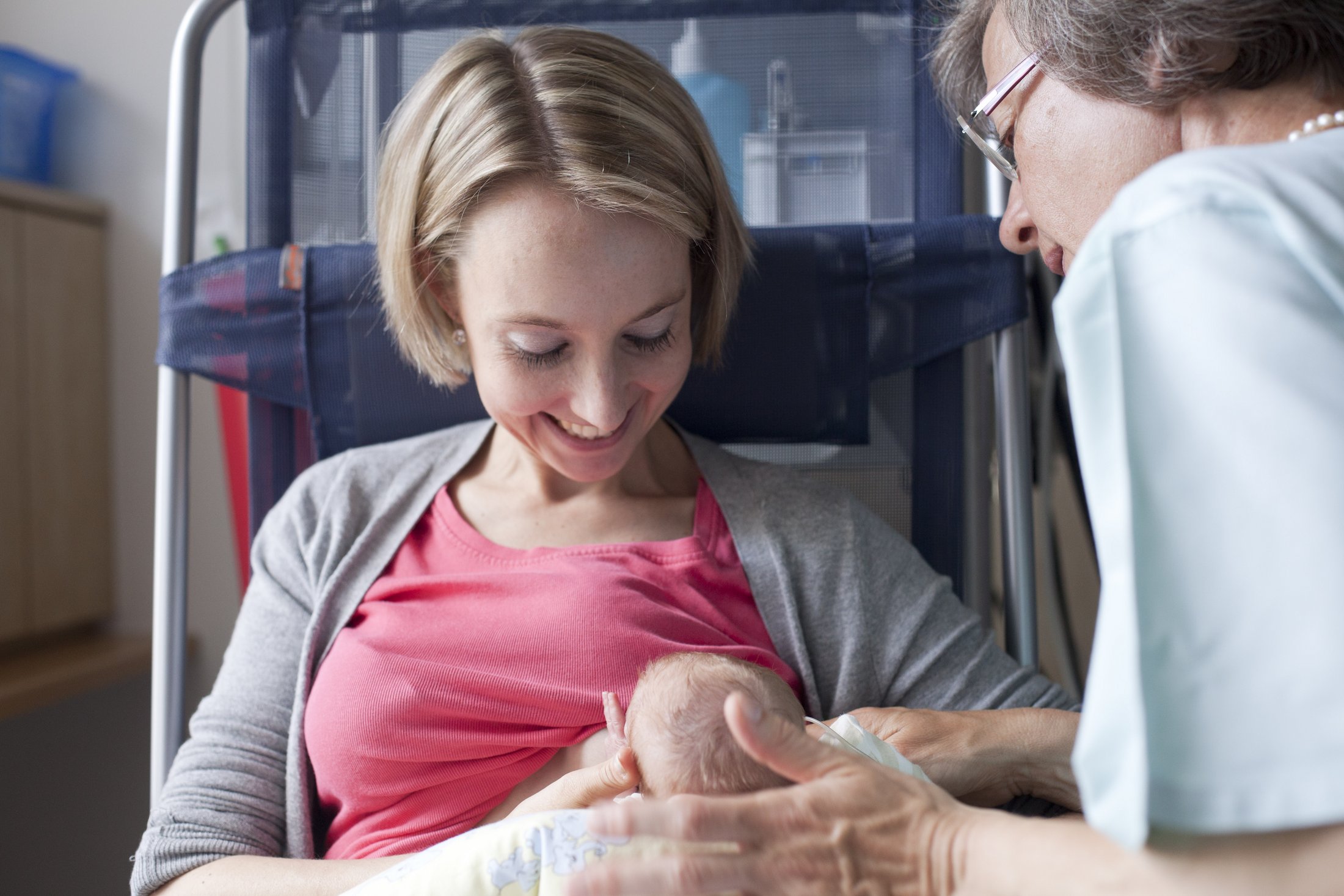Mother breastfeeding her baby in the NICU while a healthcare professional offers support.