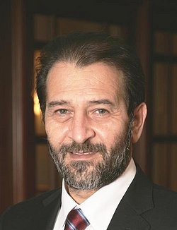 Portrait of Kypros Nicolaides in a suit with bookshelf background.
