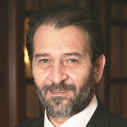 Portrait of Kypros Nicolaides in a suit with bookshelf background.