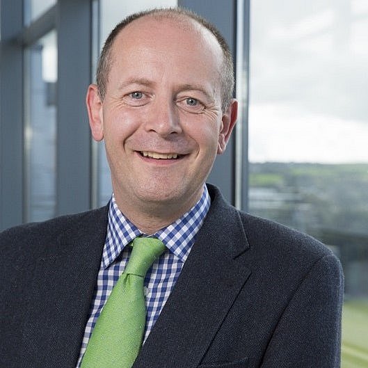 Portrait of Dr. Daniel Nuzum smiling and wearing a suit with a green tie. 