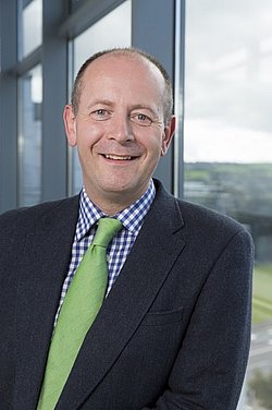 Portrait of Dr. Daniel Nuzum smiling and wearing a suit with a green tie. 