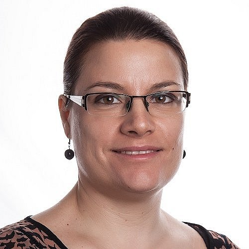 Professional Portrait of Nina Nikolova in a patterned blouse wearing glasses, looking confident.