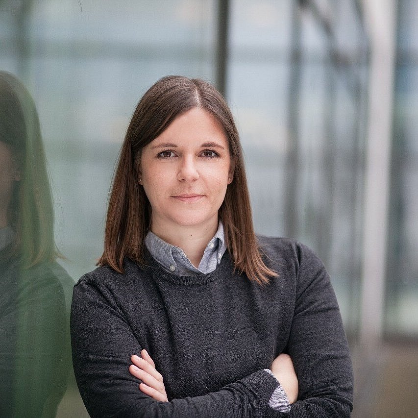 A professional headshot of Dr. Julia Feiler, standing confidently near a modern glass building.