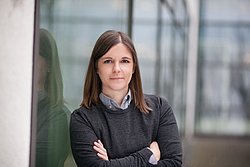 A professional headshot of Dr. Julia Feiler, standing confidently near a modern glass building.