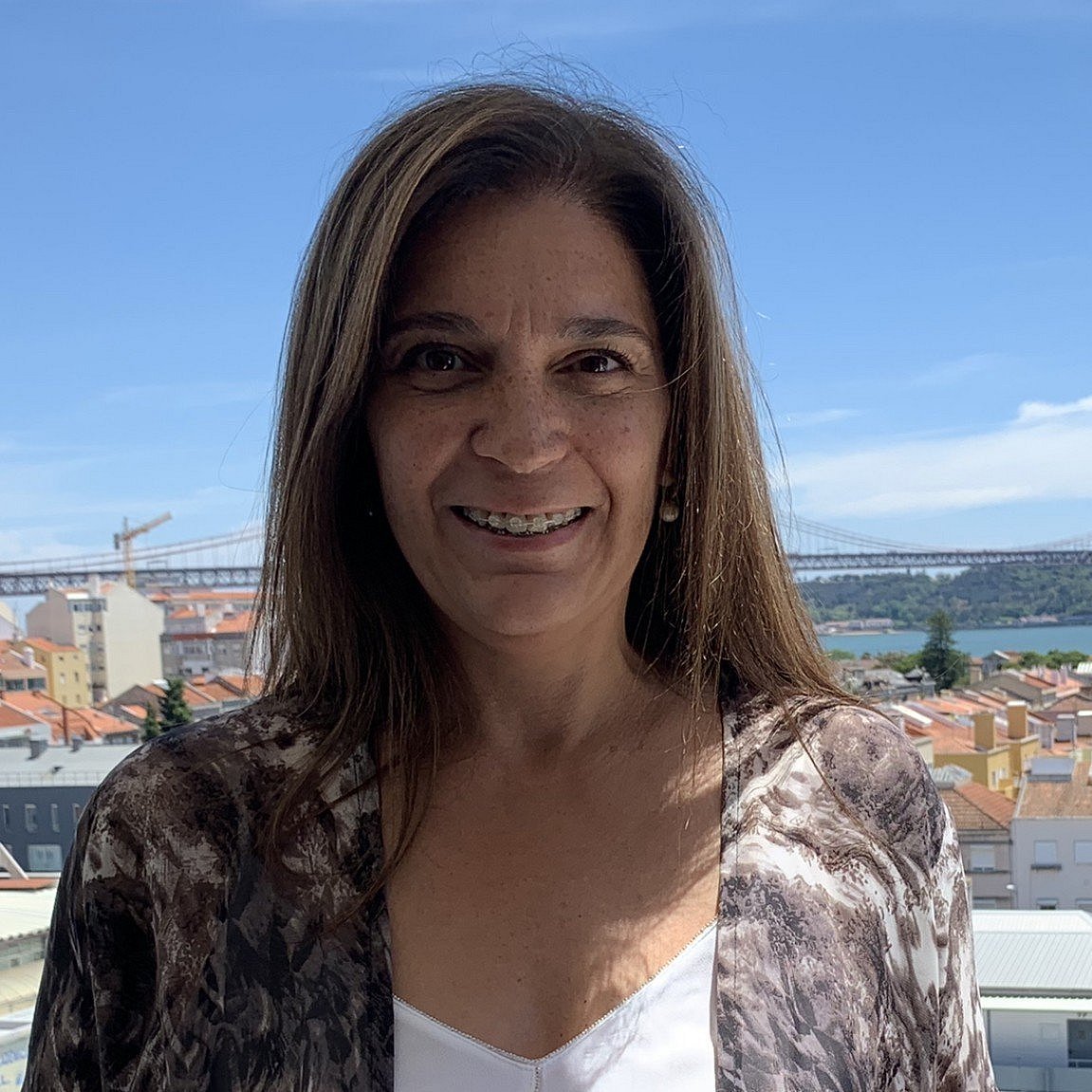 Portrait of Paula Guerra smiling in front of a scenic cityscape.