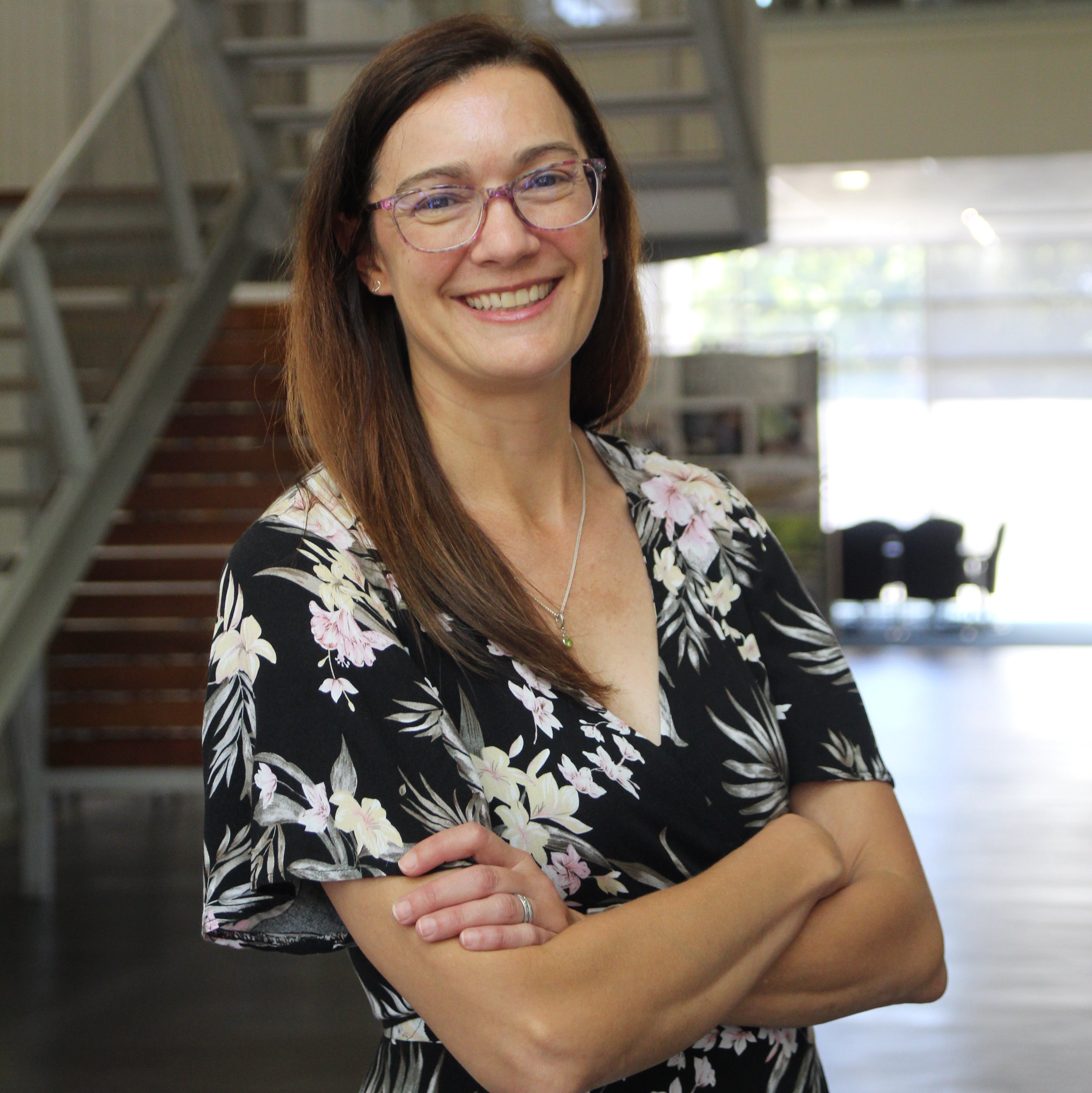 Portrait of Dr. Mary Kinney smiling in front of a metal staircase and wearing a floral dress. 