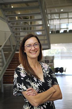 Portrait of Dr. Mary Kinney smiling in front of a metal staircase and wearing a floral dress. 