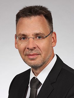 Portrait of Professor Mario Rüdiger wearing a black suit and a black tie.