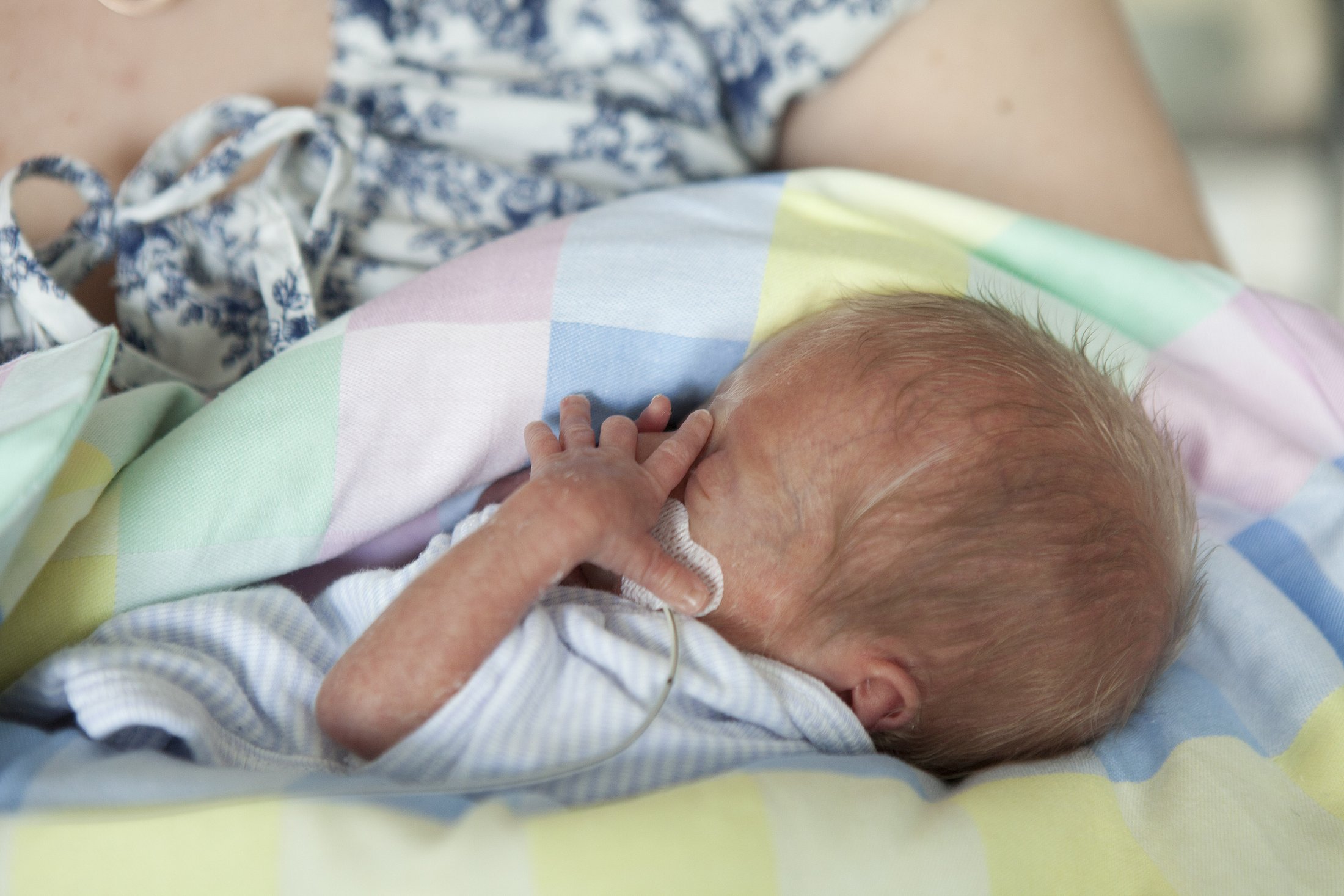 Preterm Infant Resting Close to a Caregiver Small preterm infant resting close to a caregiver on a pastel-colored blanket with a medical tube visible.