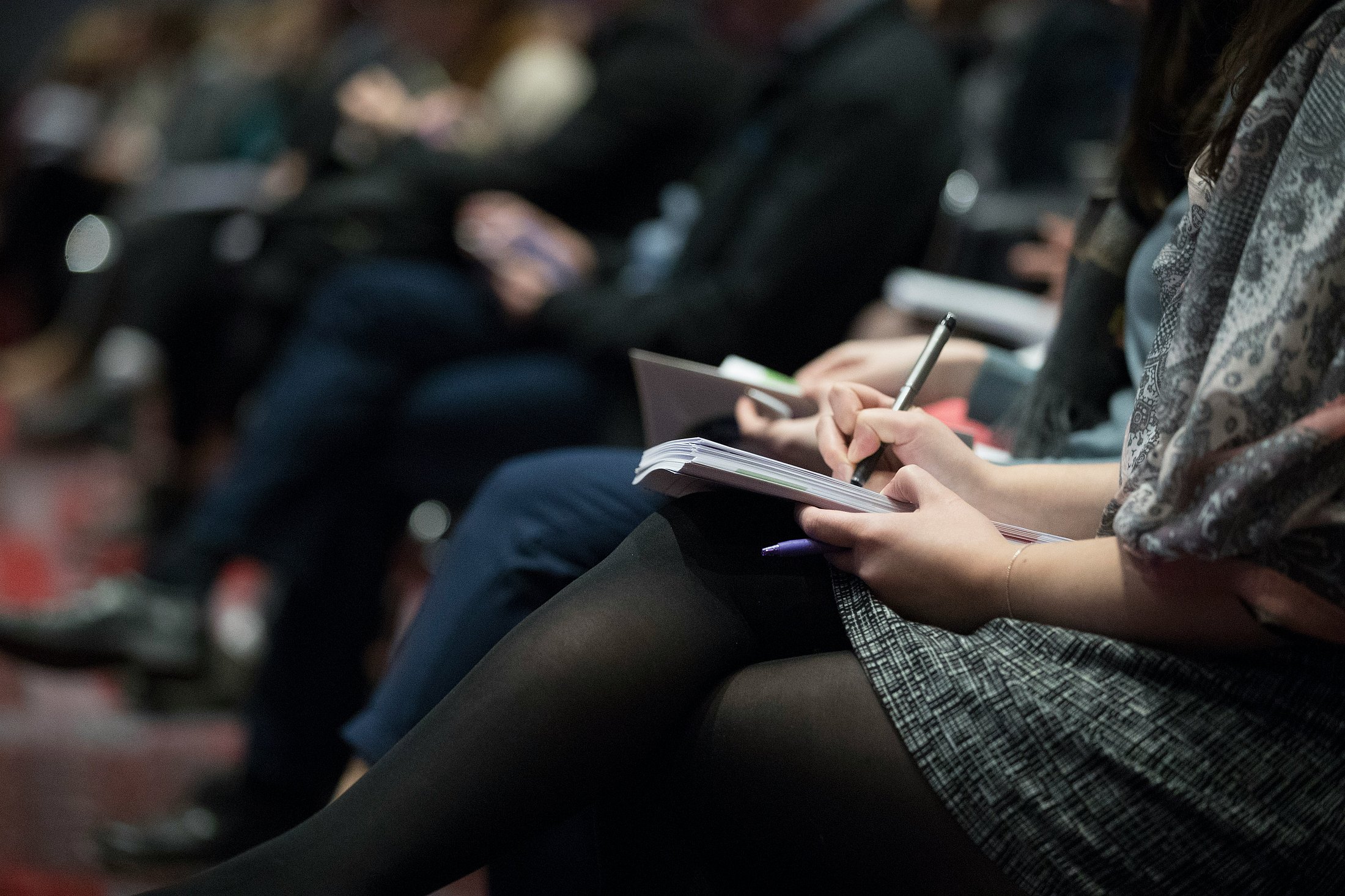 Participants taking notes during a professional event Close-up of participants writing notes in notebooks during a professional conference or workshop.