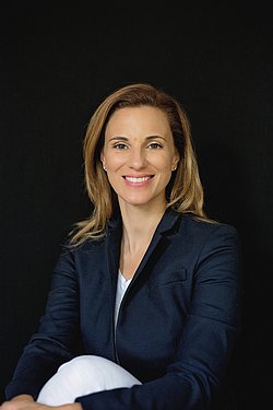 Fabiana Bacchini Fabiana Bacchini smiling in a black blazer with a dark background.