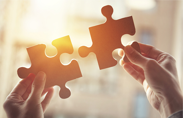 Two hands holding puzzle pieces together against sunlight, symbolising teamwork and making a difference.