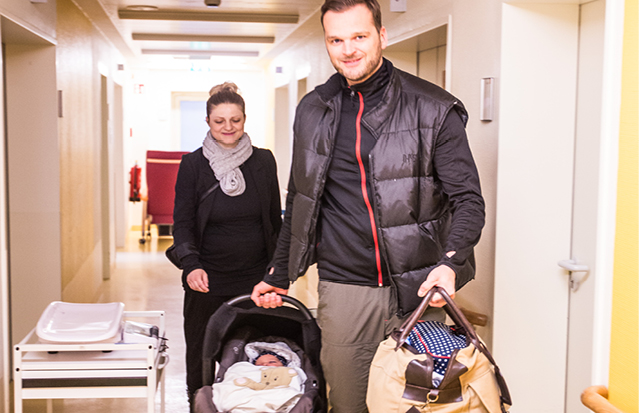Parents carrying their newborn in a car seat while leaving the hospital.