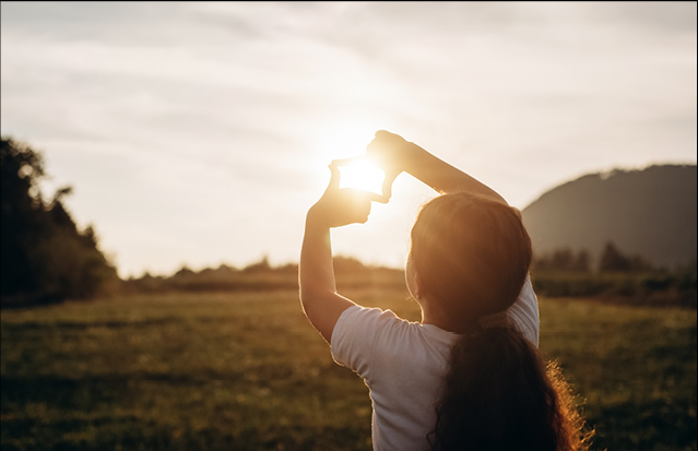 A child forming a frame with their hands around the sun, looking toward the future.