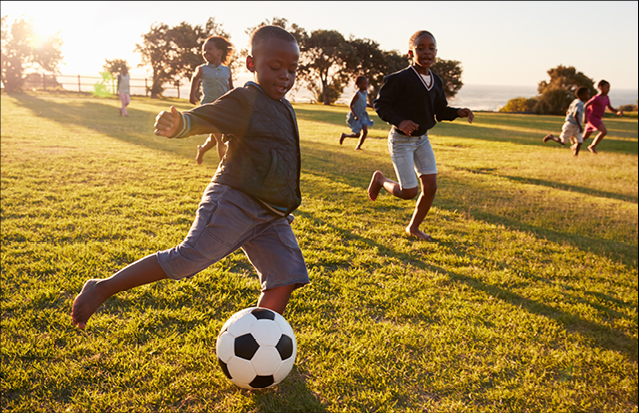 Several children running and playing in a grassy field under the sun.