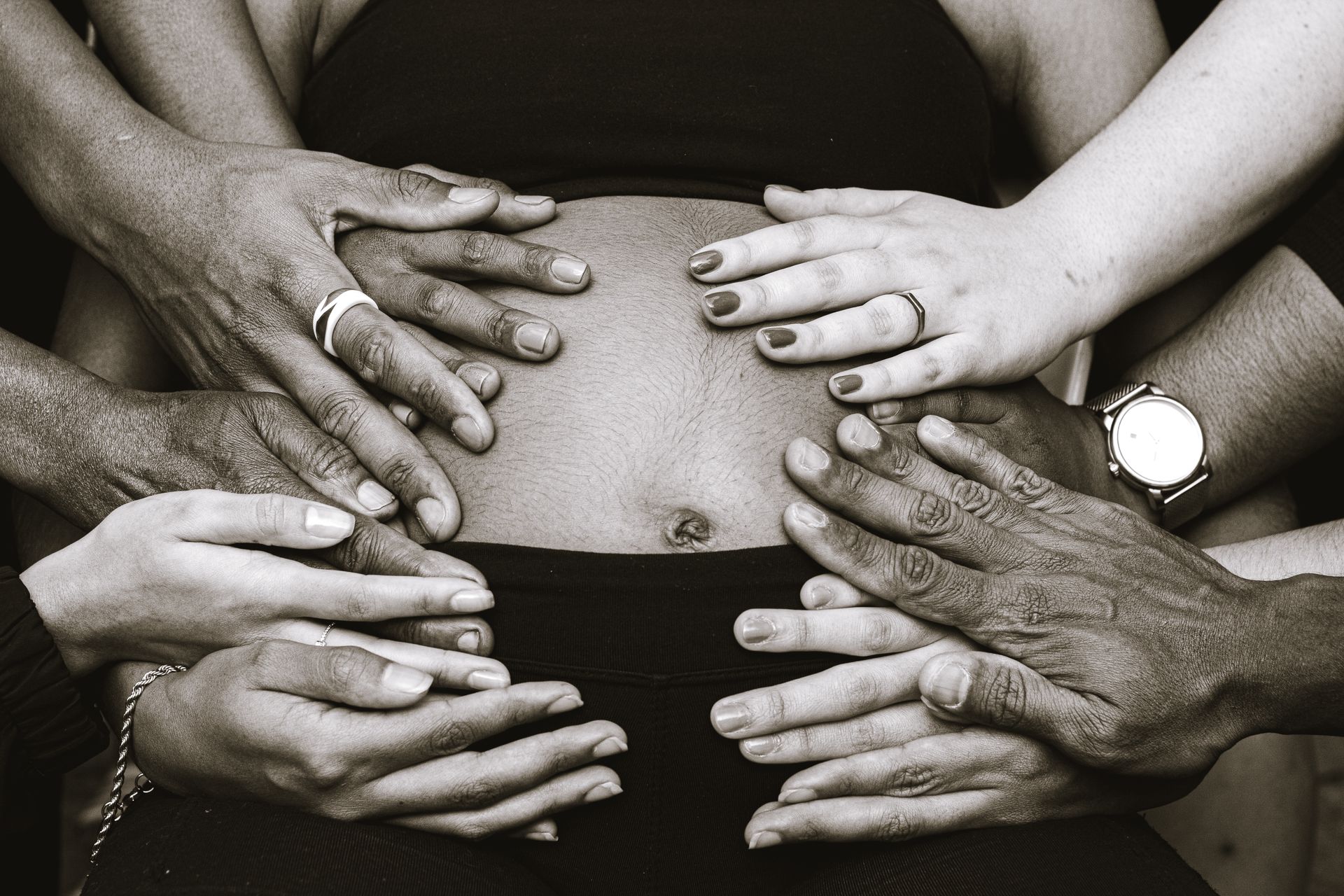 Community and Family Support During Pregnancy Several diverse hands placed around a pregnant person’s belly in a gesture of support.