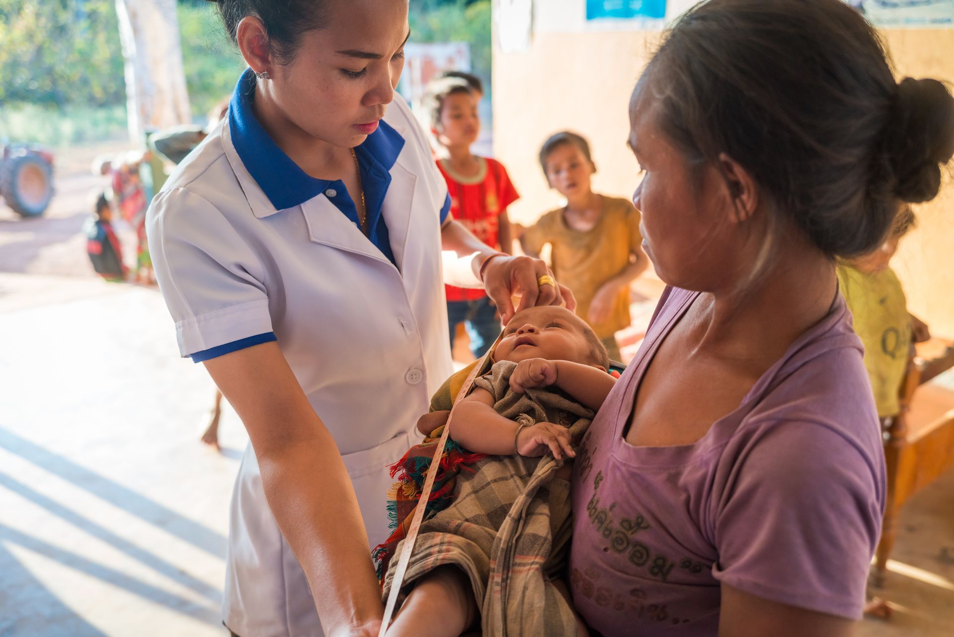 Newborn Health Assessment in a Community Clinic Healthcare professional measuring a baby held by the mother during a community health visit.