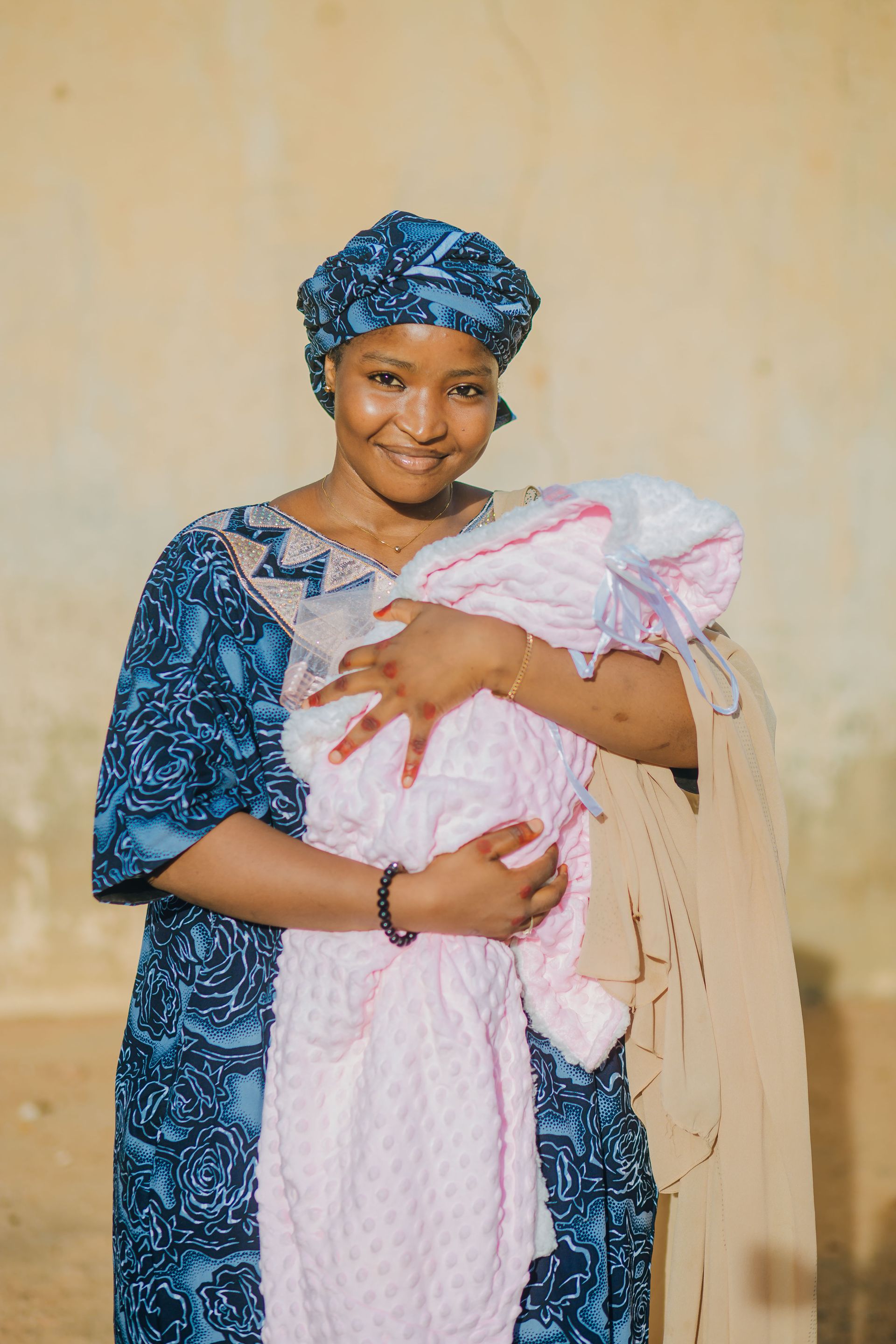 Mother Holding Her Newborn After Birth Mother wearing a blue patterned dress and headwrap while holding her newborn baby.