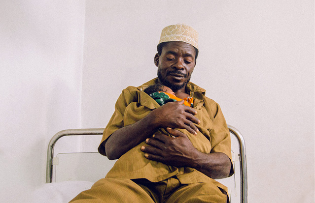 A father in a brown shirt holding his newborn in skin-to-skin kangaroo care.