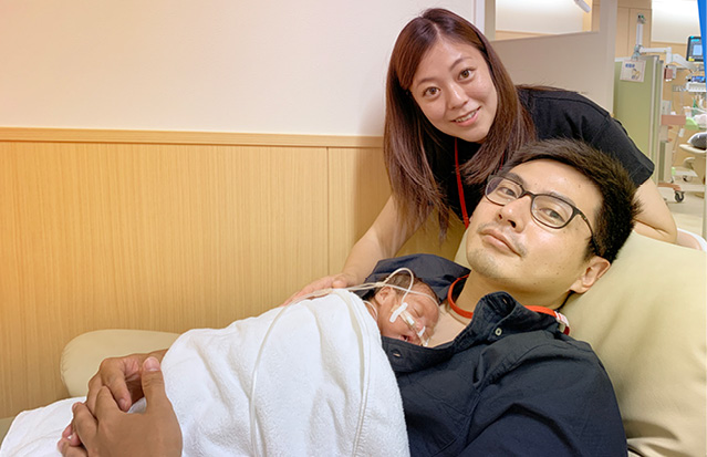 A mother and father holding their newborn in the NICU, smiling at the camera.