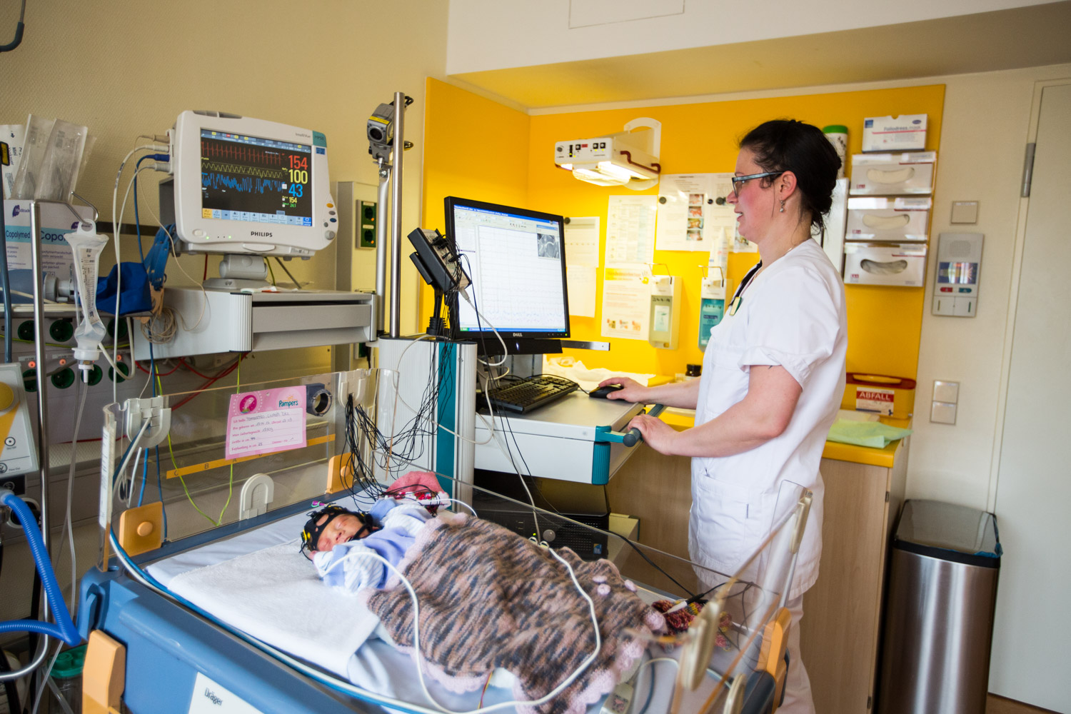 Neurological Monitoring in Neonatal Care Healthcare professional monitors a preterm infant connected to neurological and vital-sign monitoring equipment in a neonatal unit.