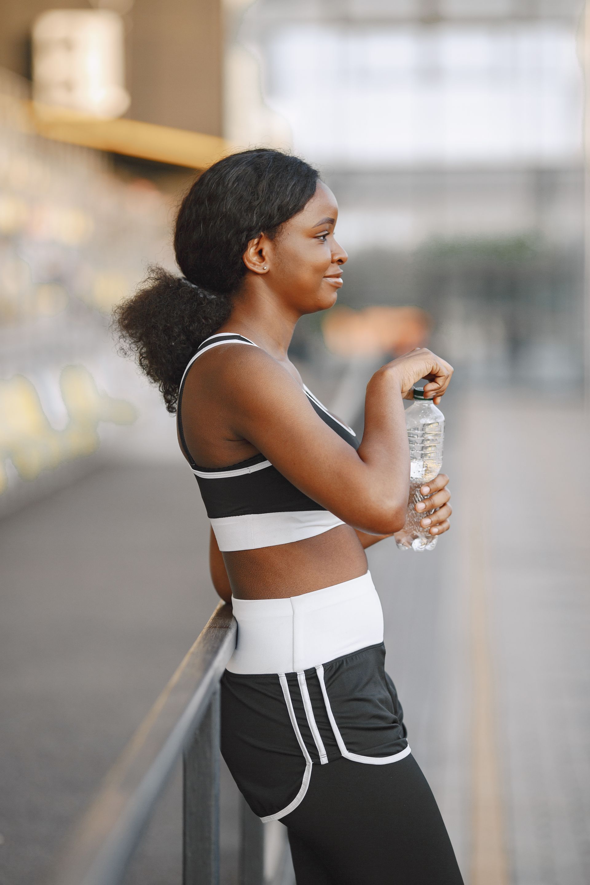Physical Activity and Maternal Wellbeing Woman wearing sportswear rests beside a railing while holding a bottle of water.