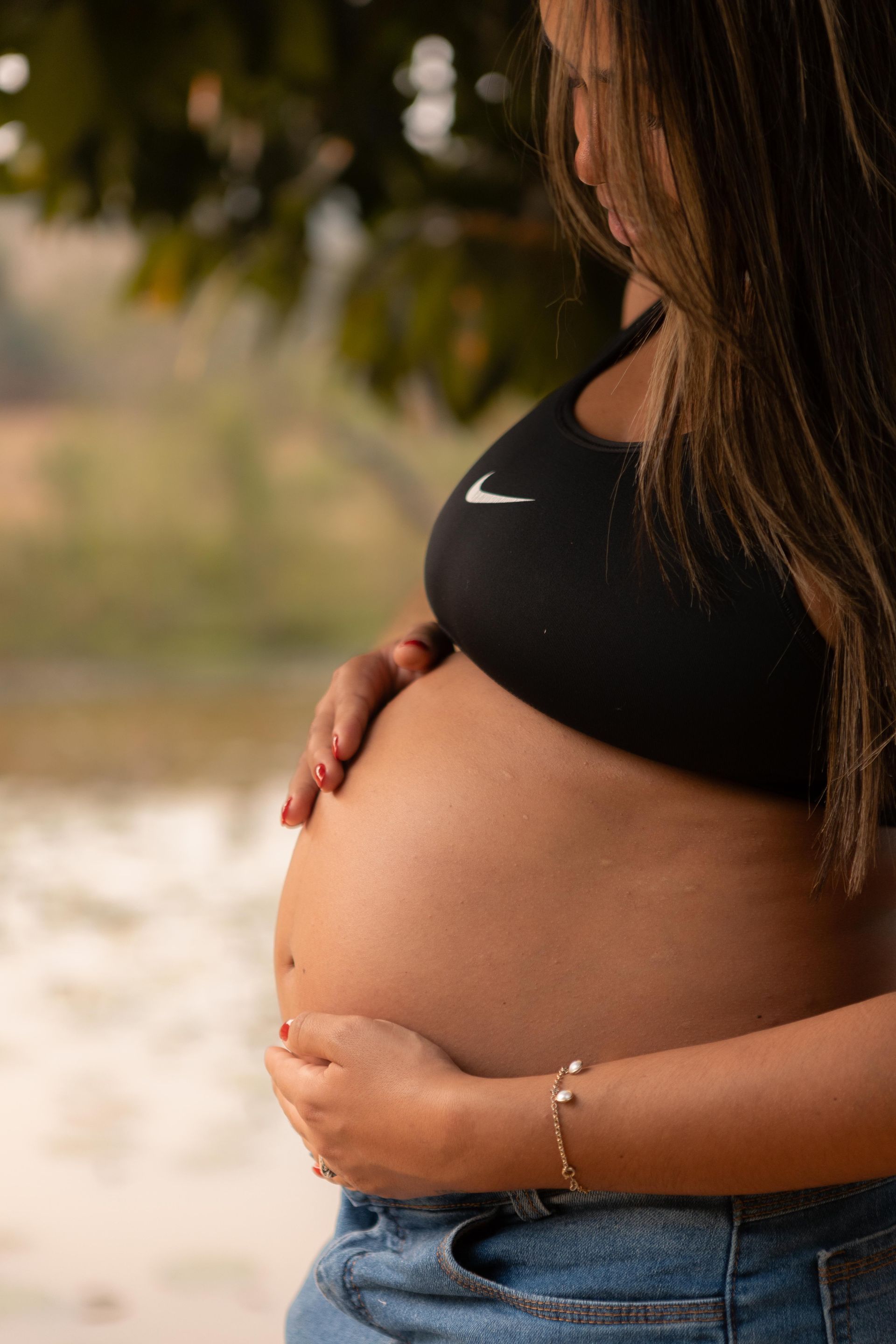 Pregnancy and Maternal Health Pregnant woman outdoors gently holding her abdomen with both hands.