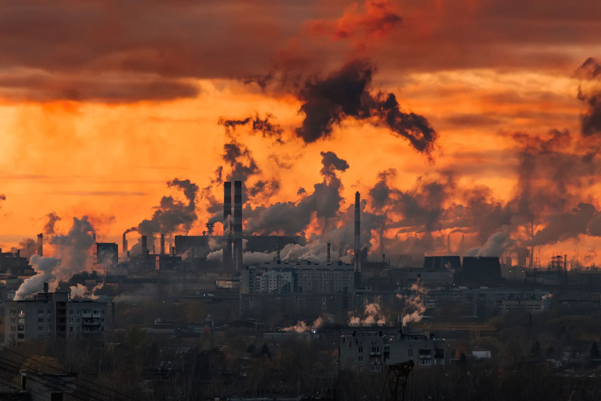 Air Pollution and Preterm Birth Risk Industrial buildings and smokestacks release heavy emissions beneath an orange sky.
