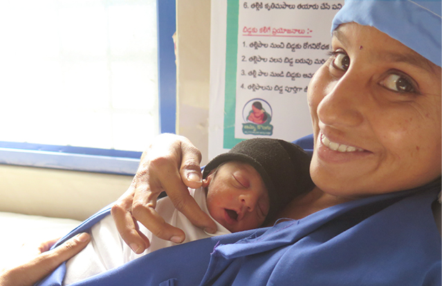 A woman wearing a blue medical gown holding her newborn in a skin-to-skin position.