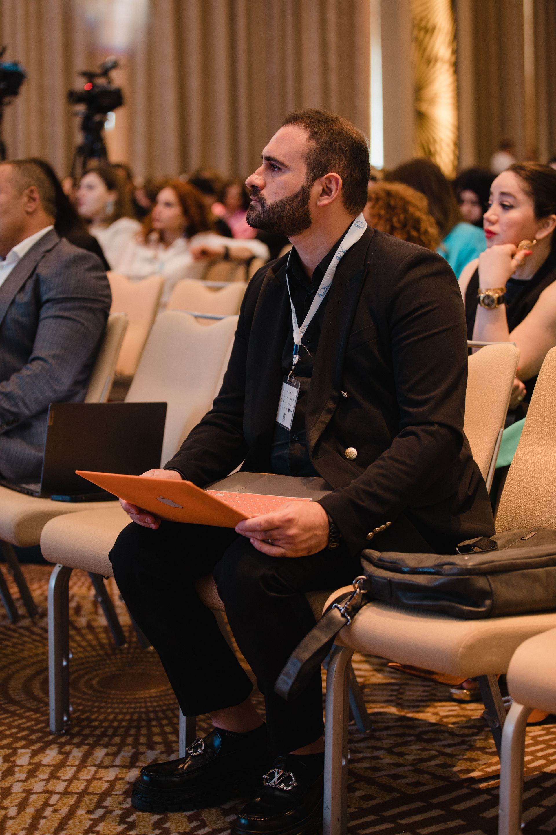 Conference attendee listening during a professional event Conference attendee holding a laptop and listening attentively during a professional event.