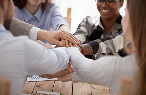 A close-up of several hands placed on top of each other as a symbol of support and trust.