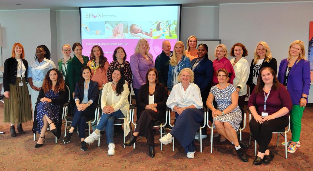 A group of diverse participants poses together at the EFONI Policy and Advocacy Workshop on RSV, with a presentation screen in the background and smiling attendees seated and standing.