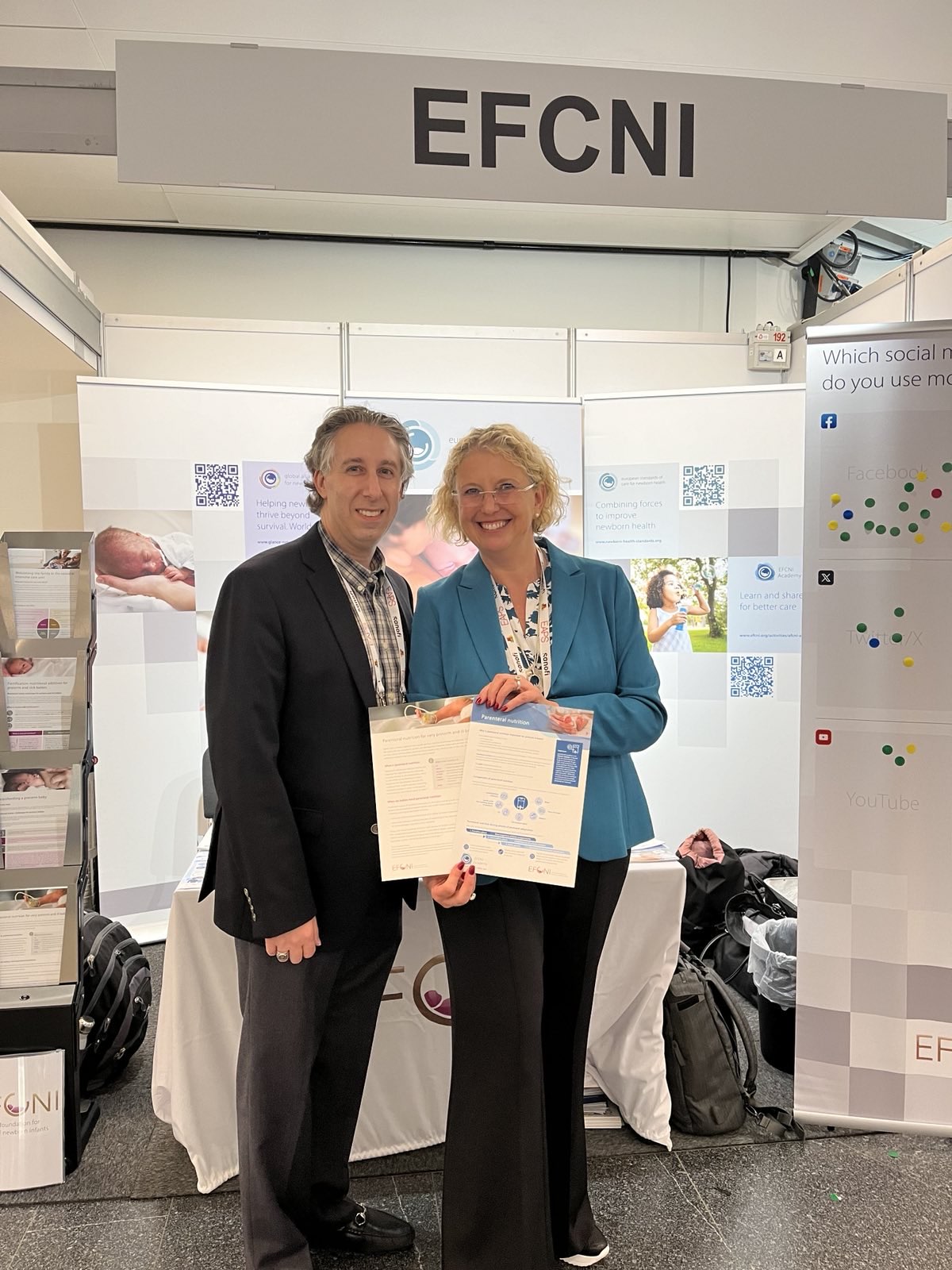 Two individuals at the EFCNI stand holding an informational leaflet on neonatal care, smiling for a photo at a health congress.
