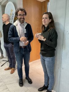 Two attendees chat over coffee at a neonatal workshop, standing near an event banner in a relaxed setting.