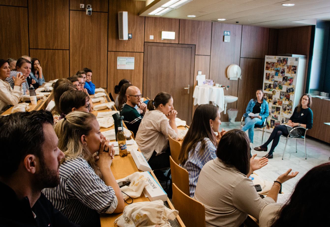 Participants in a Swiss peer support workshop listen attentively and engage in discussion about neonatal and family-centered care.